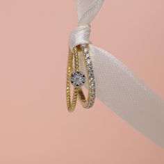 two rings tied together with a white ribbon on top of a pink background and one ring has a diamond in the middle