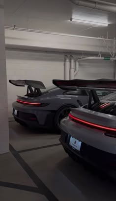 two grey sports cars parked in a parking garage next to each other with their doors open