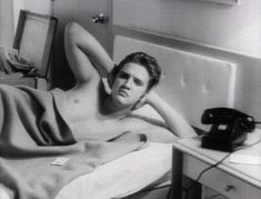 black and white photograph of a man laying in bed with an old telephone on the nightstand