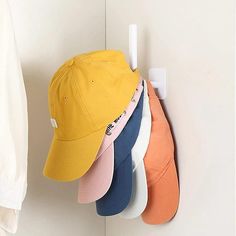 five hats hanging on the wall next to a coat rack with hat hangers in different colors