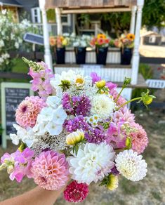 a person holding a bouquet of flowers in front of a flower shop on a sunny day