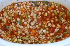 a white bowl filled with lots of different types of beans and vegetables next to a wooden spoon