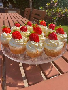 cupcakes and strawberries on a glass plate sitting on a wooden table outdoors