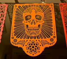 an orange paper cut out of a sugar skull hanging from a string on a wall