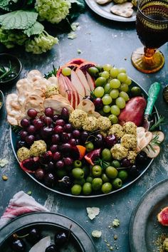 a platter full of grapes, apples, and other fruits on a table with wine glasses