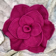 a crocheted pink flower laying on top of a white fur covered bed cover