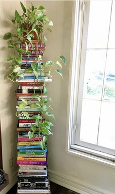 a tall stack of books sitting on top of a wooden floor next to a window