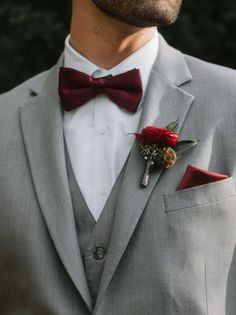 a man wearing a gray suit and red bow tie with flowers in his lapel