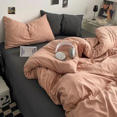 an unmade bed with pink sheets and headphones on it, next to a checkered floor