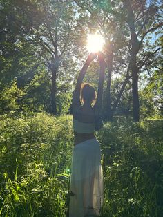 a woman is standing in the grass with her arms up to the sun behind her