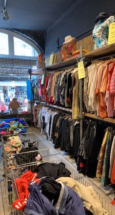 a shopping cart filled with lots of clothes next to a store shelf full of t - shirts