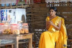 a woman in a yellow sari sits on a chair and looks at the camera