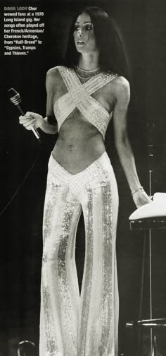 an old photo of a woman in white clothing holding a microphone and standing on stage