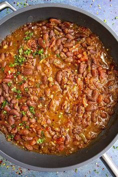 a pan filled with beans and vegetables on top of a blue countertop next to silver utensils