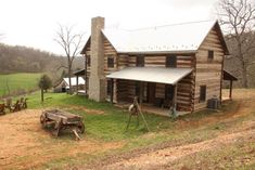 an old log cabin sits in the middle of a grassy field next to a wooden wagon