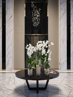 white flowers in vases sitting on a black table with marble flooring and chandelier