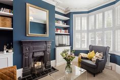 a living room filled with furniture and a fire place under a large window covered in shutters