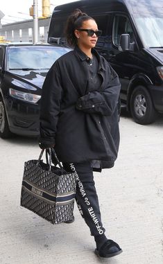 a woman walking down the street carrying a black handbag in her right hand and looking off into the distance