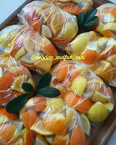 oranges and lemons wrapped in plastic sitting on a wooden platter with leaves