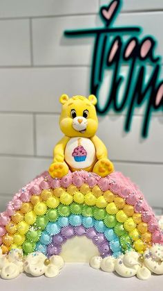 a yellow teddy bear sitting on top of a rainbow cake