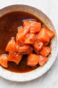 a white bowl filled with cooked salmon and brown sauce on top of a marble table