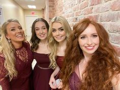 four young women are smiling and posing for the camera in front of a brick wall