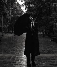 a man in a coat and tie holding an umbrella on a brick walkway next to trees