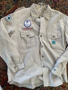 This is a vintage Scout shirt from Norway. Light gray, long sleeve and includes a Asker Og Bærum Krets patch, Norge/flag patch, and 1.Hovik patch above right breast. There are scout emblem patches on both arms and some holes where a patch was removed on the left sleeve. The inside label says HYLBAK and fabric content 73% Bomull and 27% polyester. Size label 40 . It has gray plastic scout emblem buttons.  Underarm to underarm 24" Length top of collar to hem 30" Shoulders seam to seam 18" Cotton Long Sleeve Shirt With Patches, Vintage Button-up Shirt With Patch Pockets, Vintage Long Sleeve Top With Patch Pockets, Cotton Long Sleeve Tops With Patches, Vintage Long Sleeve Tops With Patches, Scout Uniform, Uniform Shirt, Uniform Shirts, Flag Patches