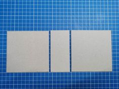 two square pieces of white paper sitting on top of a blue table with grids