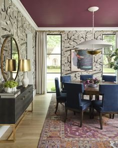 a dining room with purple walls and blue chairs in front of a wooden table surrounded by colorful rugs