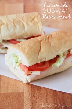 two sub sandwiches sitting on top of a white paper wrapper next to a wooden table