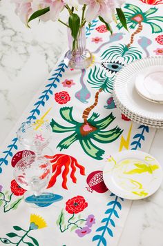 a table topped with plates and flowers on top of a white table cloth next to a vase filled with pink flowers