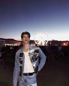 a man standing in front of a ferris wheel at night with his hands on his hips