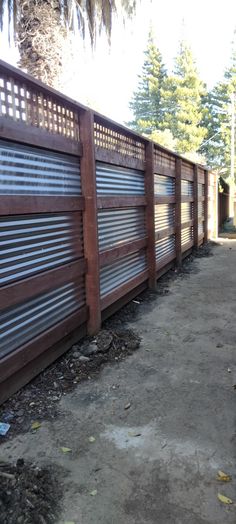 a wooden fence with metal slats on it and dirt ground in front of it