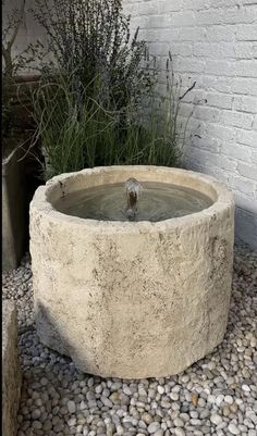 a stone water fountain in front of a white brick wall with plants growing out of it