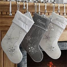 three stockings hanging from a mantel decorated with silver and white christmas decorations, along with a fireplace