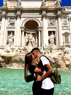 a man and woman kissing in front of a fountain