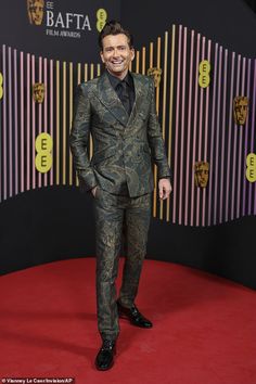 a man in a suit and tie standing on a red carpet at an awards event