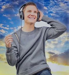 a young man wearing headphones and listening to music in front of a blue sky with clouds