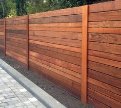 a wooden fence is shown in front of a brick walkway and sidewalk with trees on the other side