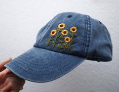 a blue hat with sunflowers embroidered on the front and side, held up by a person's hand