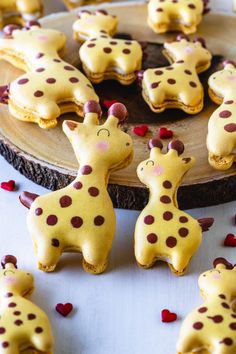 cookies decorated like giraffes are on a wooden platter and scattered with hearts