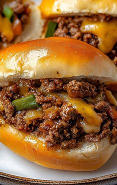 two sloppy joe sandwiches on a plate with green peppers and cheesy meat in the middle