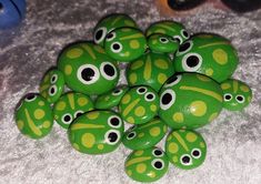 a pile of green and yellow painted rocks on a white surface with black eyes in the middle