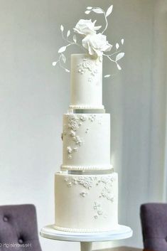 a three tiered white wedding cake on top of a wooden table with purple chairs