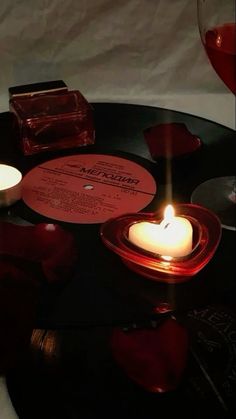 two candles are sitting on top of a table with records and wine glasses in the background