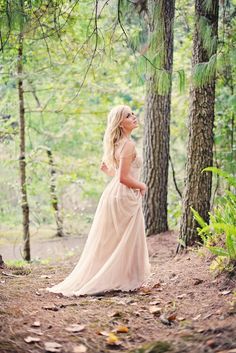 a woman standing in the woods wearing a dress and looking off into the distance with trees behind her