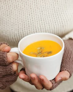 a person holding a cup of soup in their hands with both hands on the mug