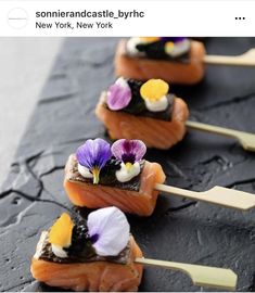 some food is laying out on a black plate and has purple pansies in the middle