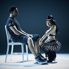 a man sitting next to a woman on top of a chair in front of a dark background